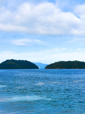 Seascape with two islands covered with dense vegetation. Calm turquoise water in the foreground. Clear sky with fluffy white clouds. Tropical peace and serenity.の写真素材