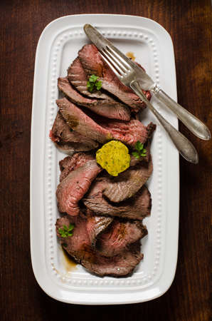 Juicy roast beef slices on white plate on cutting board with herb butterの写真素材