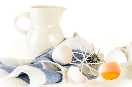 Baking ingredients and tools: eggs, flour, jug of milk, whisk and kitchen towel