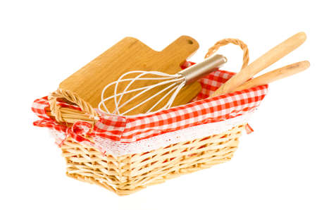 Kitchen tools in the basket, consisting of whisk, cutting board, wooden salad spoons, isolated on whiteの写真素材