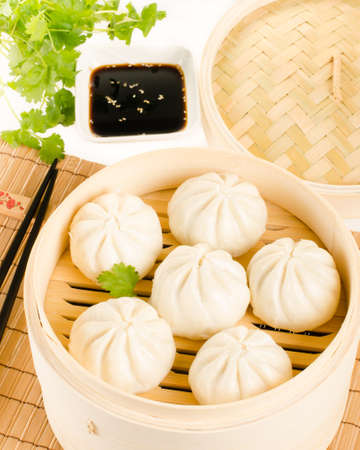 Chinese steamed buns in bamboo steamer basket with cilantro, soy sauce and chopsticks on whiteの写真素材