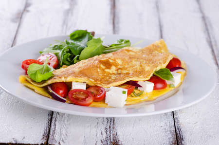 Omelette with cherry tomatoes and feta cheese on white wooden background