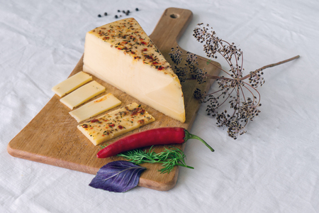 Homemade cheese with herbs and spices (red pepper and seeds) on a kitchen board.の写真素材