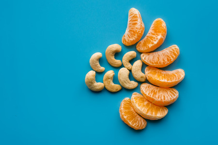 Mix ripe mandarin slices and cashew on blue background. Isolated fruit and nut. Healthy diet concept.の写真素材