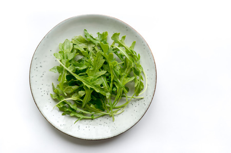 Fresh italian rucola leaves (arugula) on rustic plate. White background. Top viewの写真素材