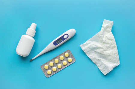 Medical equipment on blue background. Digital thermometer, nasal spray, drugs. Top view.