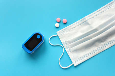 Portable pulse oximeter, pills and face mask on blue background. Covid-19, healthcare concept. Top view.の写真素材