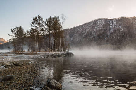 Bank of the Yenisey River in the Sayan mountains. Light fog over the river. The stones are covered with ice. Khakassia. Siberia.の写真素材