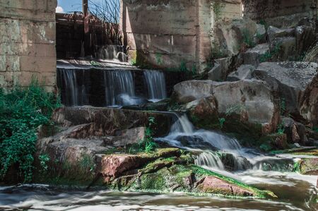 Small waterfall under the dam with rapids frome stones and green moss in long exposure