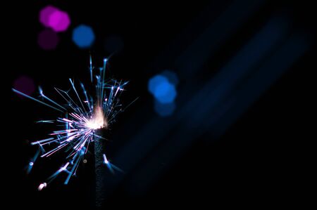Burning sparkler in blue and white light on a black background. Closeup photo of Christmas and new year sparkler. Can be used like a wallpaper or postcard.の写真素材