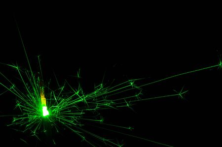 Burning sparkler in green and white light on a black background. Closeup photo of Christmas and new year sparkler. Can be used like a wallpaper or postcard.の写真素材