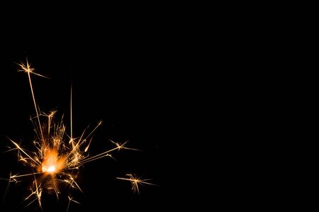 Burning sparkler in yellow and orange light on a black background. Closeup photo of Christmas and new year sparkler. Can be used like a wallpaper or postcard.の写真素材