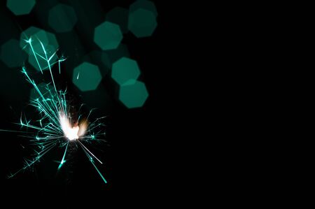 Burning sparkler in turquoise and white light on a black background. Closeup photo of Christmas and new year sparkler. Can be used like a wallpaper or postcard.の写真素材
