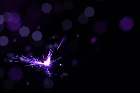 Burning sparkler in violet and white light on a black background. Closeup photo of Christmas and new year sparkler. Can be used like a wallpaper or postcard.の写真素材