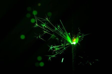 Burning sparkler in green and white light on a black background. Closeup photo of Christmas and new year sparkler. Can be used like a wallpaper or postcard.の写真素材