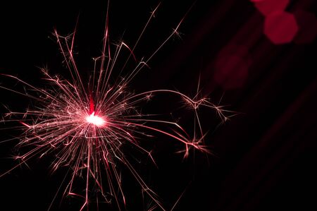 Burning sparkler in red and white light on a black background. Closeup photo of Christmas and new year sparkler. Can be used like a wallpaper or postcard.の写真素材