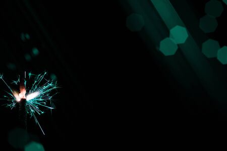 Burning sparkler in turquoise and white light on a black background. Closeup photo of Christmas and new year sparkler. Can be used like a wallpaper or postcard.の写真素材