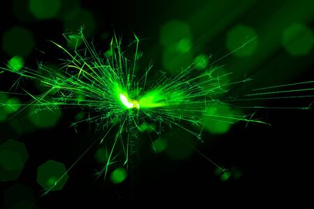 Burning sparkler in green and white light on a black background. Closeup photo of Christmas and new year sparkler. Can be used like a wallpaper or postcard.の写真素材