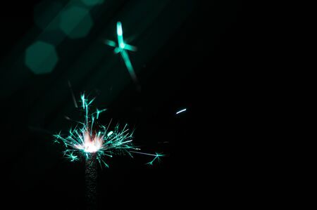 Burning sparkler in turquoise and white light on a black background. Closeup photo of Christmas and new year sparkler. Can be used like a wallpaper or postcard.の写真素材