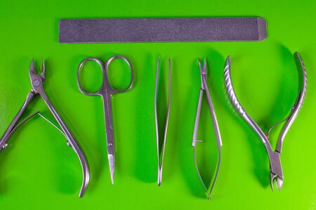 Manicure and pedicure tools on green background. Nail file, scissors, tweezers pusher, nippers. Medical tools top view.の写真素材