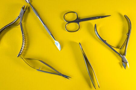 Manicure and pedicure tools on yellow background. Nail file, scissors, tweezers pusher, nippers, tassels. Medical tools top view.の写真素材