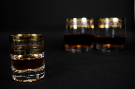 Short Glass of dark red whiskey, brandy or bourbon isolated on black background. Closeup photo of...