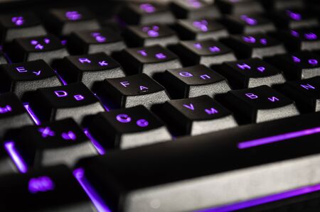 Abstract background of black computer keyboard with violet backlight. Closeup photo with bokeh, can be used like a wallpaper.の写真素材