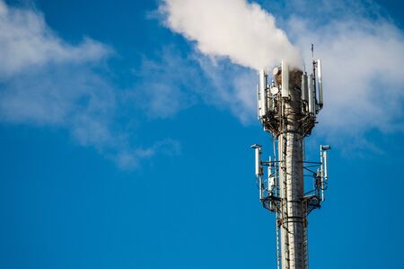 A boiler room tower with radio antennas and mobile antennas on a background of a blue sky with white...