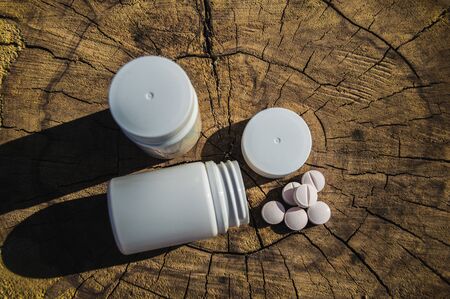 White jar and white pills lie on a stump. Pills or tablets closeup with bokeh.