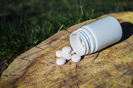 White jar and white pills lie on a stump. Pills or tablets closeup with bokeh.の写真素材