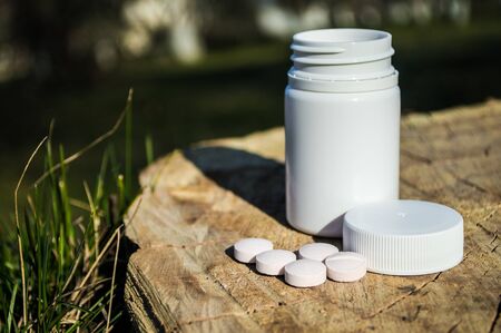 White jar and white pills lie on a stump. Pills or tablets closeup with bokeh.