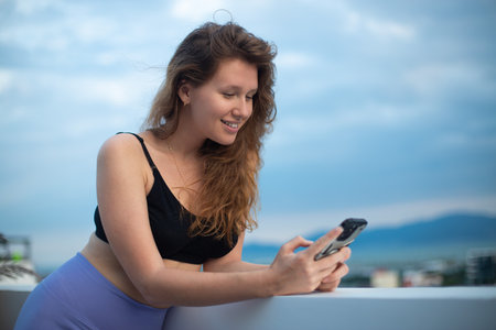 happy young girl uses her phone on the roof of a house, balcony, city background, a woman taking...