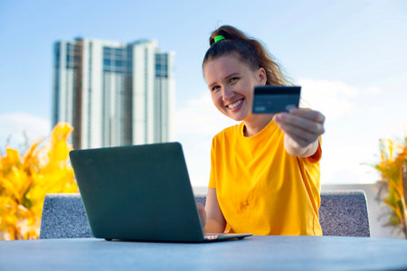 Young beautiful attractive happy satisfied woman with credit bank card and laptop computer outdoors...