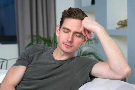 Young relaxed handsome calm man is resting, relaxing at home with closed eyes in living room,...