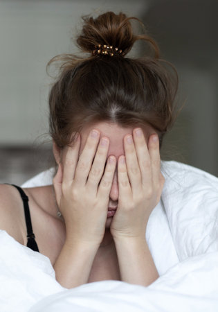 young unhappy depressed girl, beautiful lazy lonely woman covering herself in blanket, suffering from depression with sad upset frustrated look at home in living room in early morning. Vertical photoの写真素材