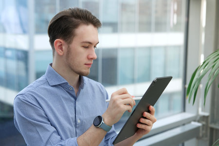 Young man, office worker or student is using tablet computer, device with electronic pen or pencil, drawing or writingの写真素材