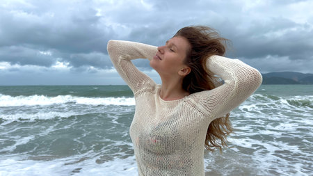 Portrait of beautiful girl, young happy positive cheerful joyful woman enjoying vacation on sea, ocean, walking on summer beach in tropical country, smiling, having fun, laughing in knitted sweaterの写真素材