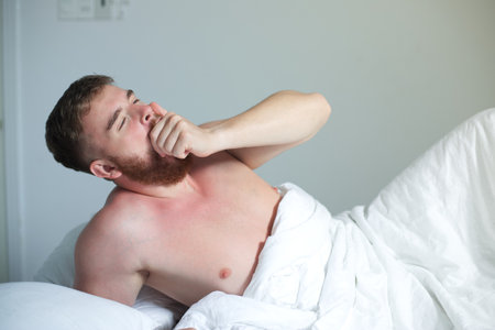 Young happy handsome sleepy man in the bed in bedroom at home in the morning lying under white...