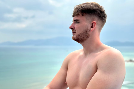 handsome and sporty, topless guy enjoying and sunbathing in the sun on the rooftop of a lux hotel spa suite with sea,ocean view on vacationの写真素材