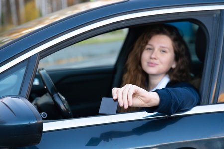 Beautiful happy cheerful girl, young positive woman is paying with credit plastic card from her car smiling, holding out bank card from opened automobile window. Payment for purchases, fast food autoの写真素材