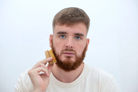 Handsome young bearded guy, European brutal man with a beard hair is combing the beard on face with...