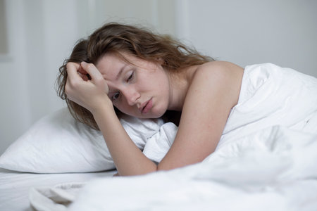 Young sad depressed unhappy worried woman in the bed in bedroom at home in the morning lying under white blanket suffer from insomnia problems with sleep at nightの写真素材