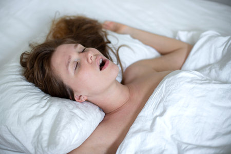 young girl sleeps in the morning in bed and snores loudly with her mouth open, the concept of person have problem with sleep and breathingの写真素材