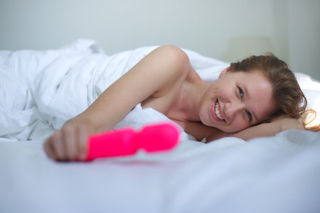 Young happy sexy woman hold in hand sex toy, masturbate with vibrator in bed in bedroom at home.の写真素材
