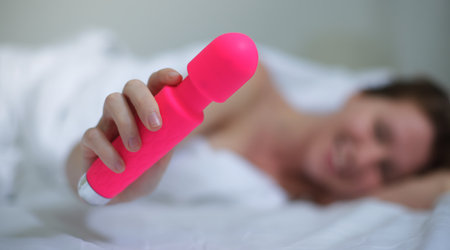 Young happy sexy woman hold in hand sex toy, masturbate with vibrator in bed in bedroom at home.の写真素材