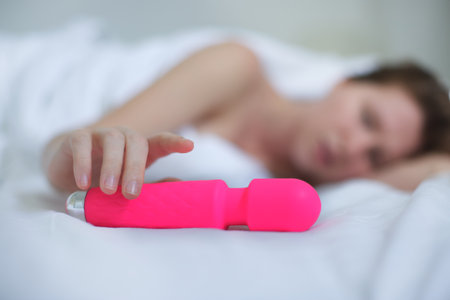 Young happy sexy woman hold in hand sex toy, masturbate with vibrator in bed in bedroom at home.の写真素材