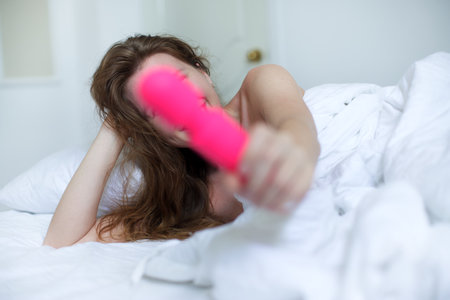 Young happy sexy woman hold in hand sex toy, masturbate with vibrator in bed in bedroom at home.の写真素材