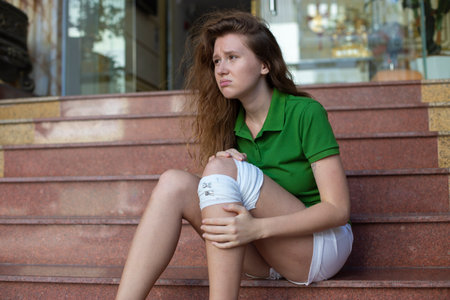 Girl with leg injury, dislocation, bandage sits on the stairsの写真素材