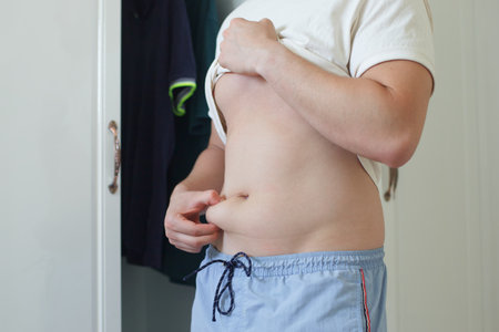 Unhappy sad upset young man with fat on her stomach, guy worried about body fat touching belly standing at home near closetの写真素材