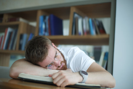 Portrait of tired overworked guy, exhausted young man in glasses college or university student is study hard in library, prepare to exam, lessonの写真素材